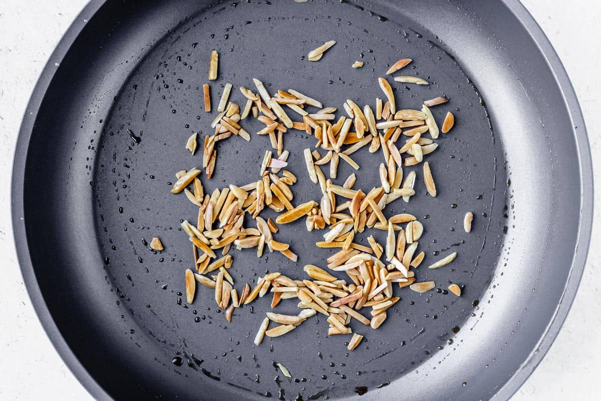 Toasted almond slivers in a gray skillet over a white background