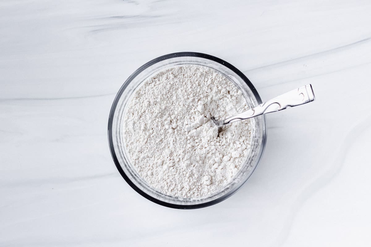 flour, baking soda and salt sifted together in a glass bowl with a spoon in it