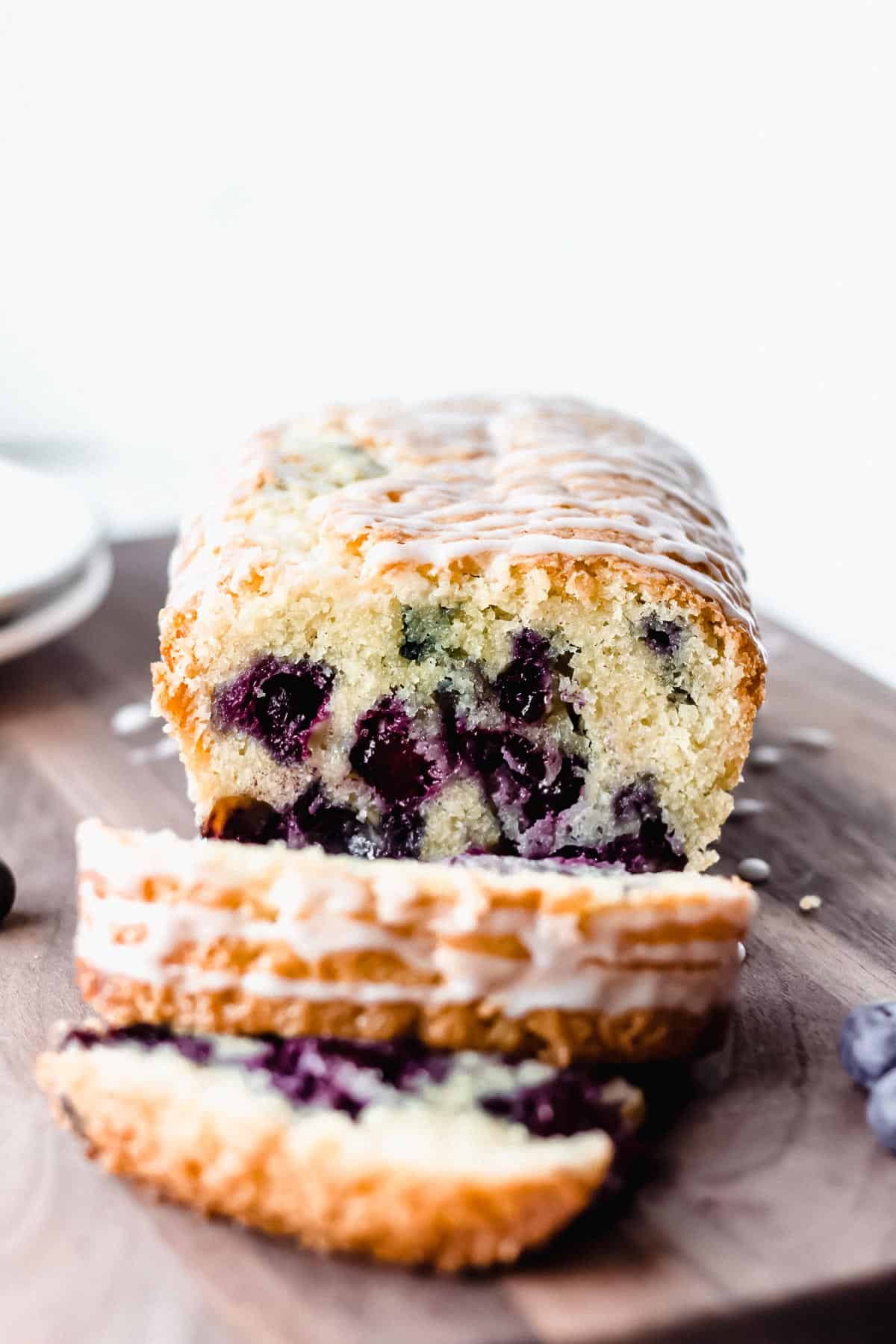 Straight on view of blueberry pound cake with 2 slices cut in front of it on a cutting board