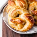 Close up of soft homemade pretzels on a white plate over a wood board