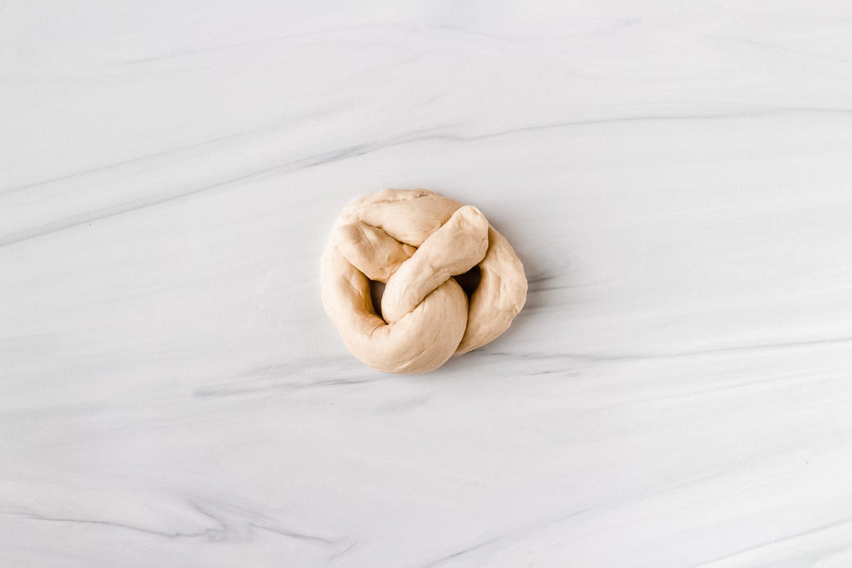 a single pretzel before baking on a white background