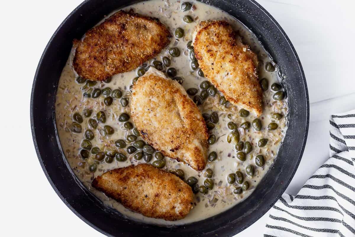 Browned chicken breasts in piccata sauce in a black skillet
