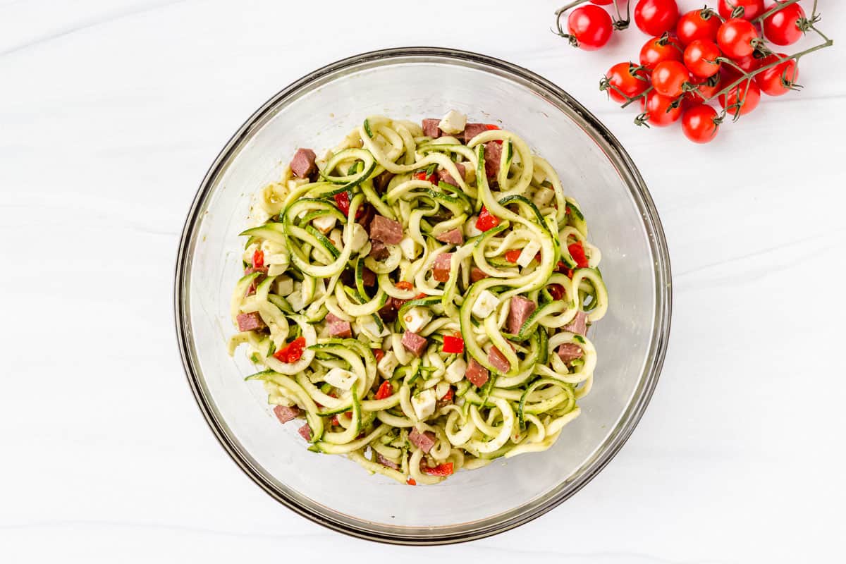 Zucchini pesto pasta salad in a glass bowl with cherry tomatoes on the vine next to it