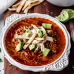 Keto Chicken Tortilla Soup in a white bowl on a wood board with lime wedges and tortilla strips in the background