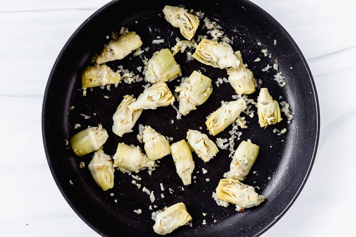 Artichokes, shallot and garlic cooking in a black skillet
