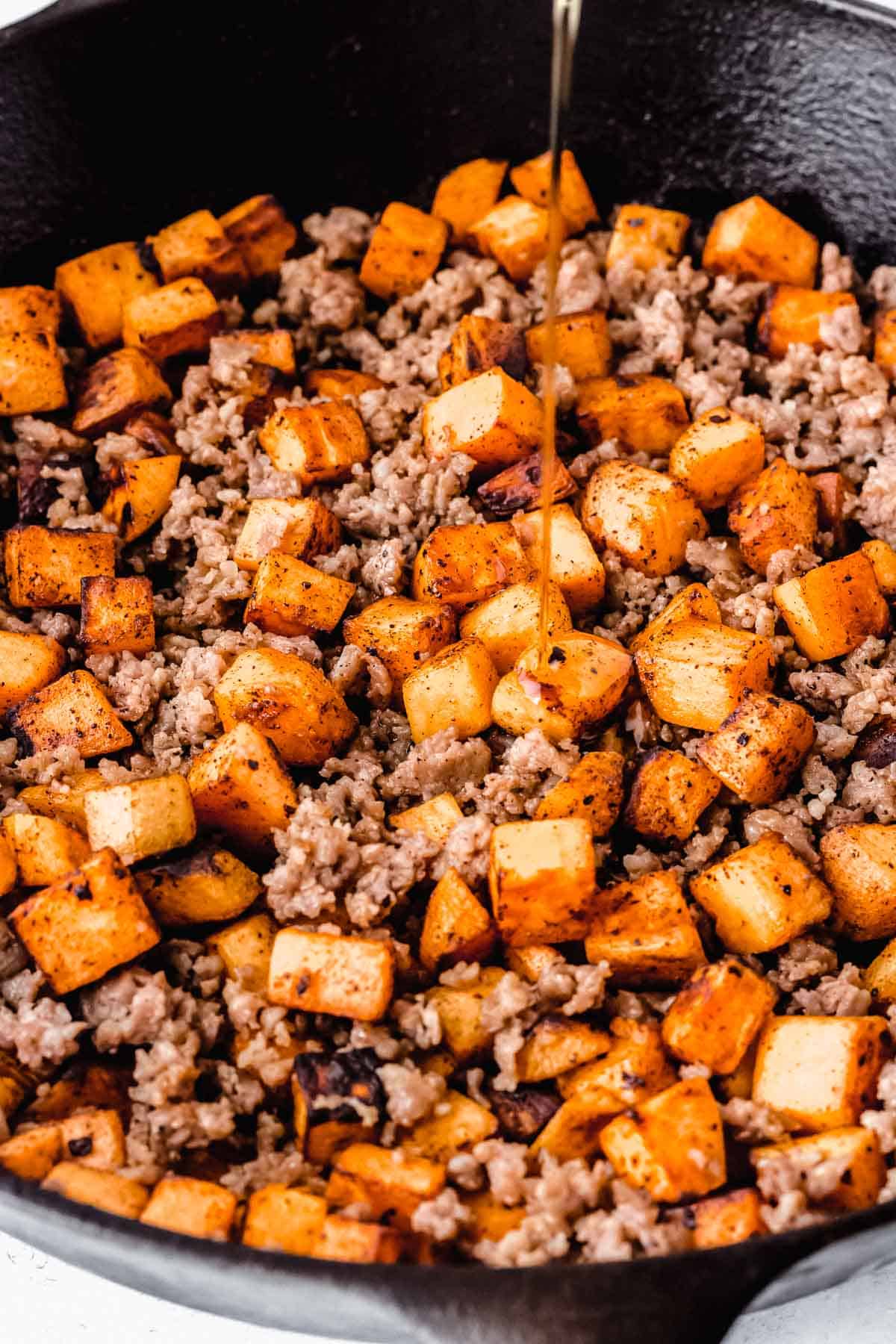 Maple syrup being drizzled over sausage and sweet potato hash