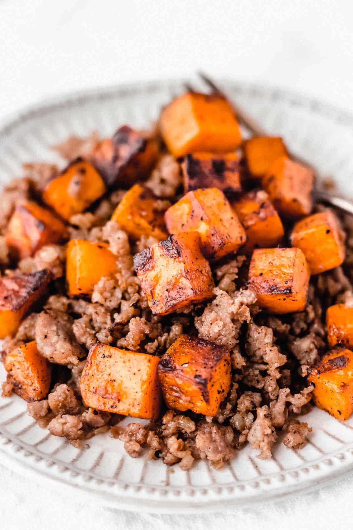 CLose up of maple sausage sweet potato hash on a white plate with a fork