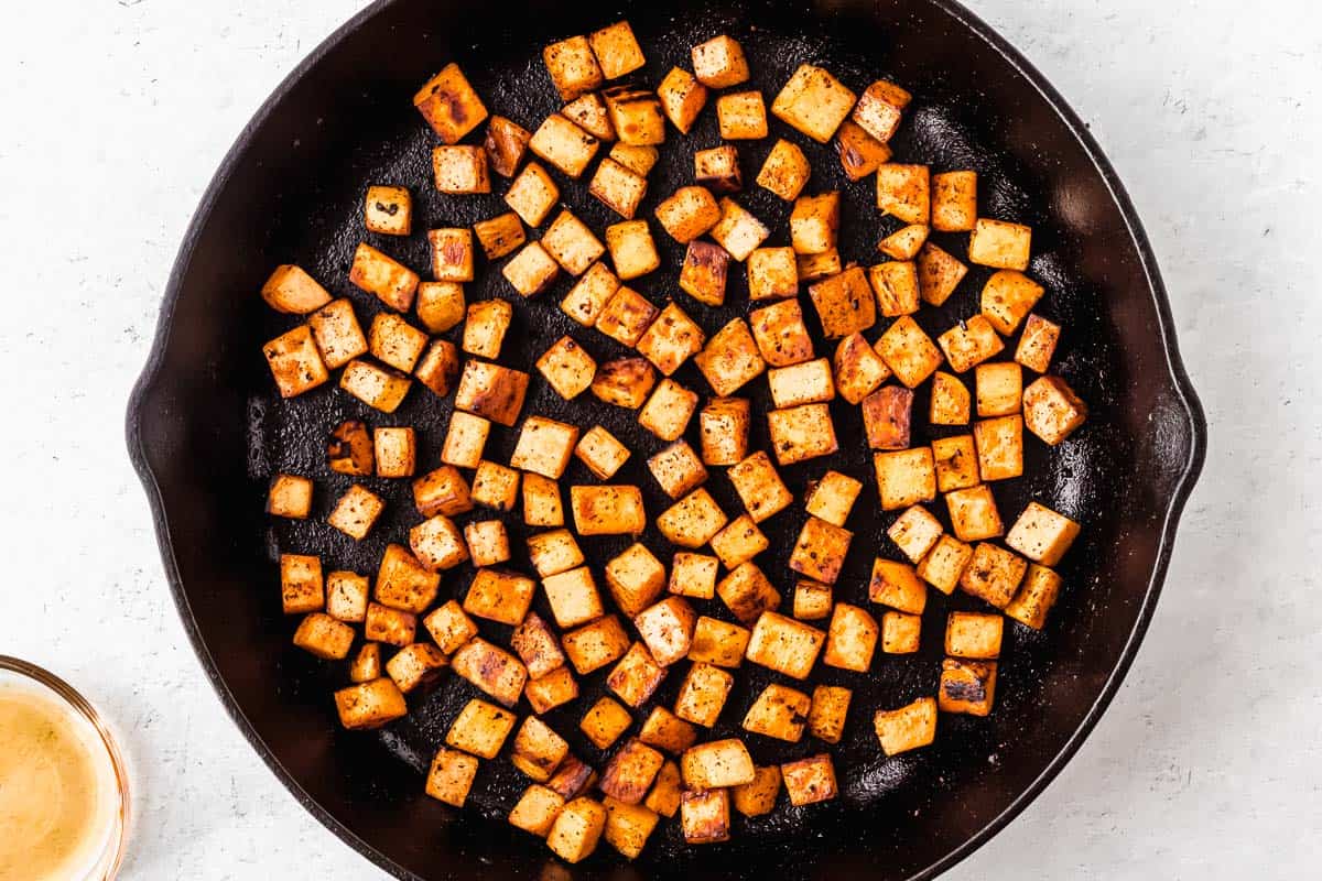 Cubes of sweet potatoes cooking in a black cast iron skillet