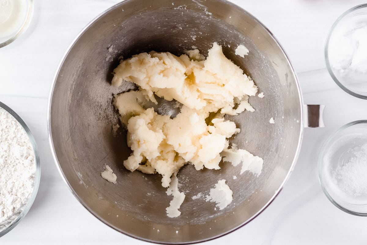 Butter and sugar creamed together in a silver mixing bowl over a white background with other ingredients around it