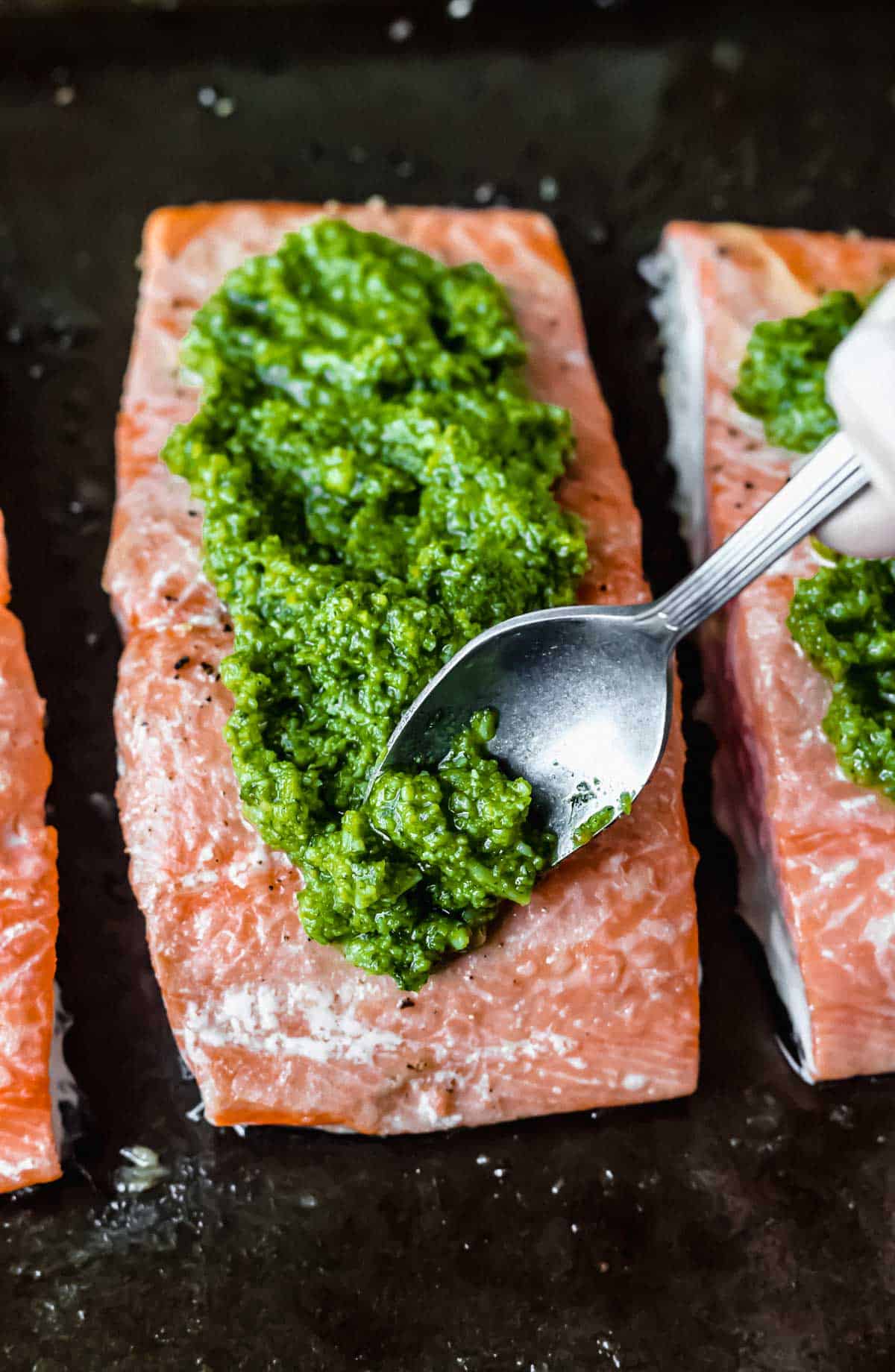 Close up of a spoon adding pesto to the top of a fillet of salmon