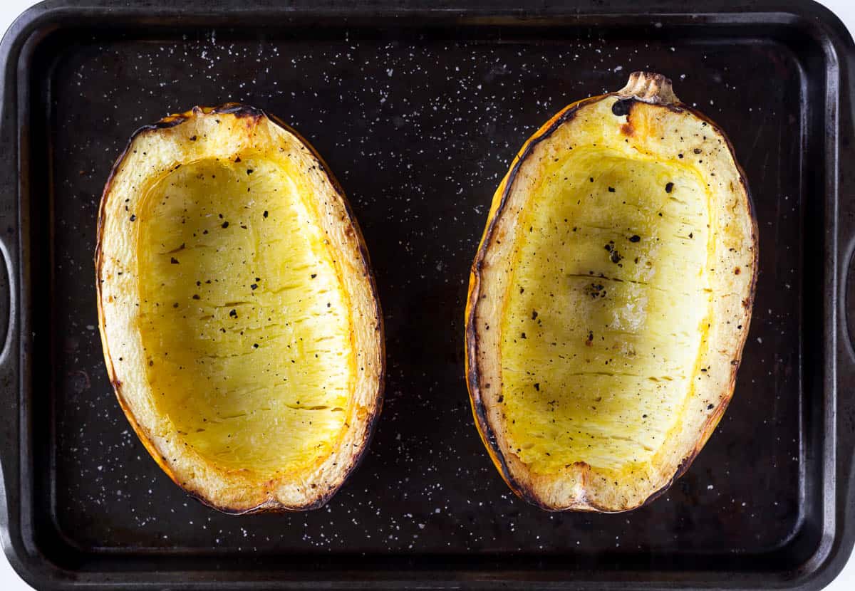Two halves of a spaghetti squash roasted on a baking sheet with salt and pepper