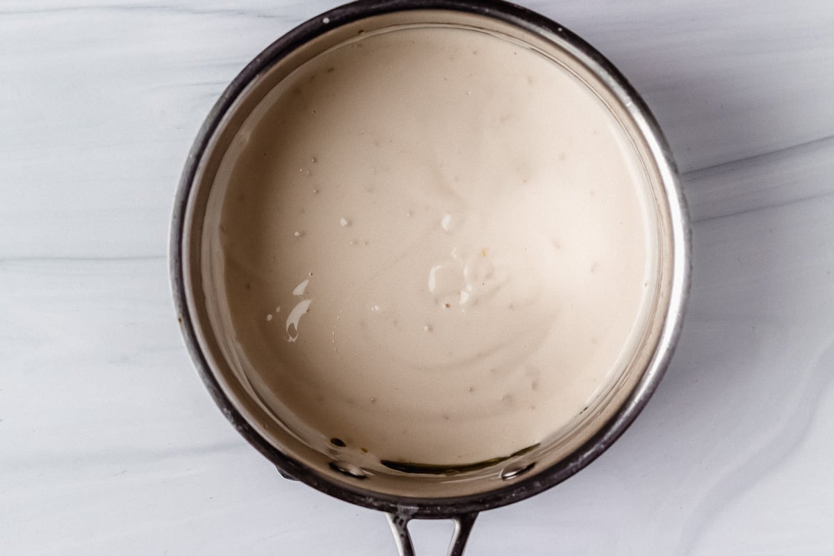 Alfredo sauce in a silver pot over a white background