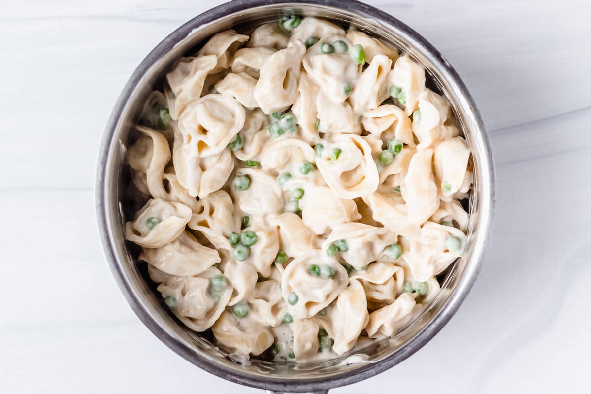 Tortellini alfredo with peas in a silver pot over a white background