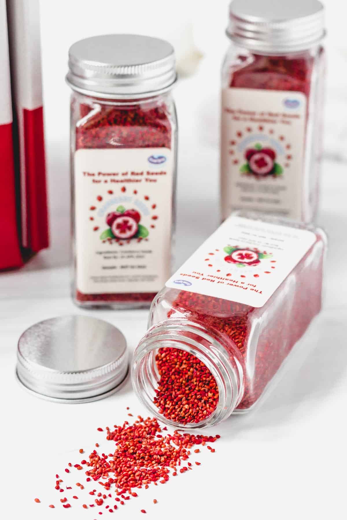 3 jars of cranberry seeds with one on its side with seeds pouring out onto a white table