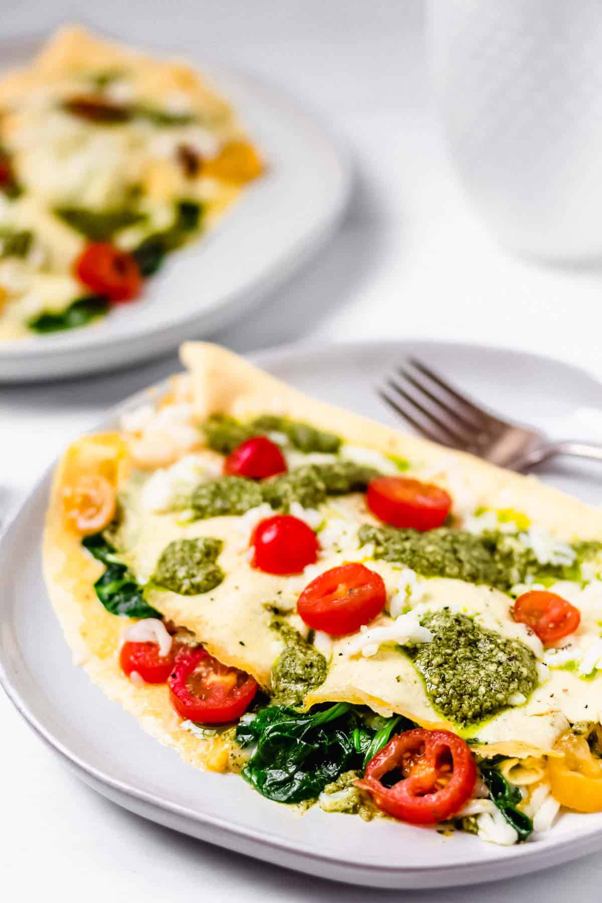 Pesto Caprese Omelet with Mozzarella Cheese and Cherry Tomatoes on white plates on a white backdrop