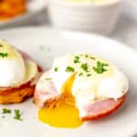 Keto eggs Benedict cut open to let the yolk run out on a white plate with text overlay.
