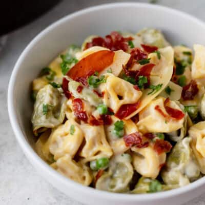 Close up of a bowl of tortellini alfredo with prosciutto and peas.