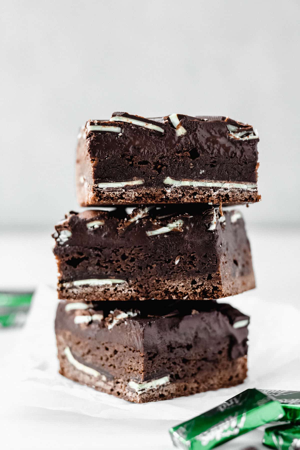 3 Andes Mint Brownies stacked on top of each other with a couple andes candies in front and in back of the stack over a white backdrop