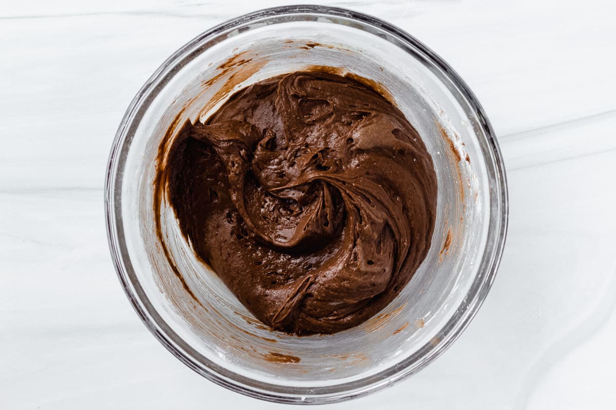 Brownie batter in a glass bowl over a white backdrop