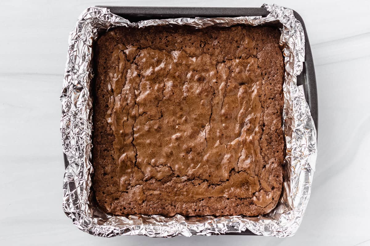 Baked brownies in a foil lined square pan over a white background