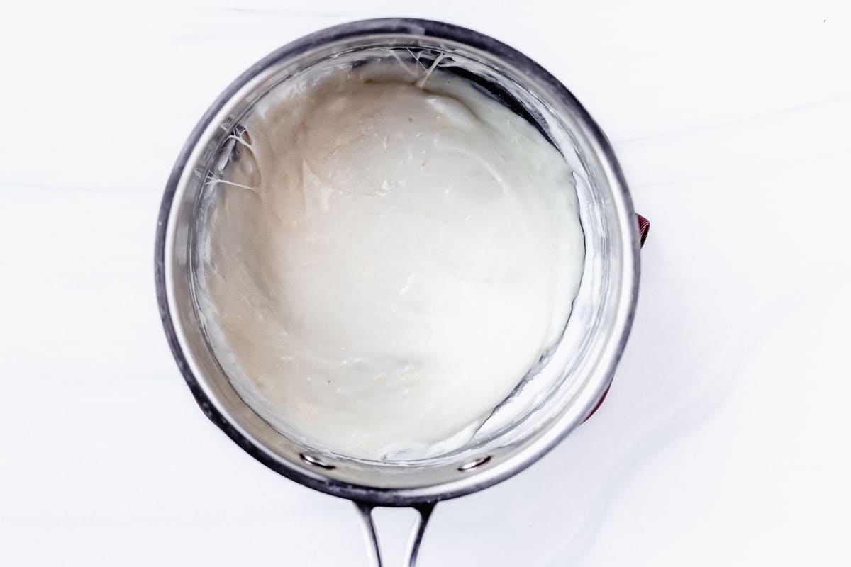 Parmesan cheese sauce in a silver pot over a white background