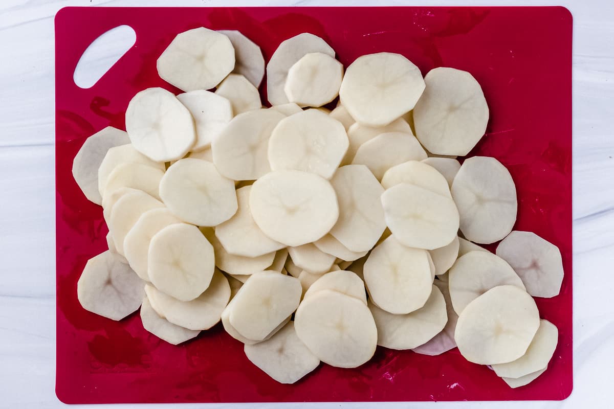 Thin sliced of potatoes on a red cutting mat