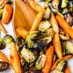 Roasted brussels sprouts and carrots with a wood turner on a baking sheet