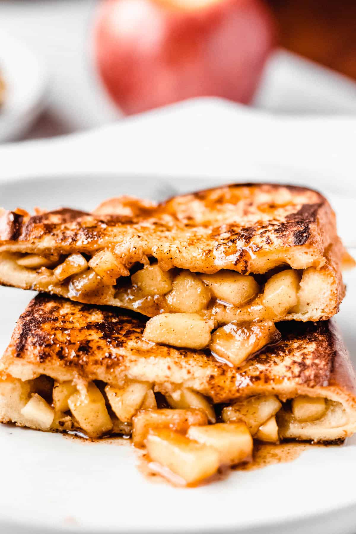 Close up of two halves of apple stuffed french toast on stacked with an apple and second plate in the background
