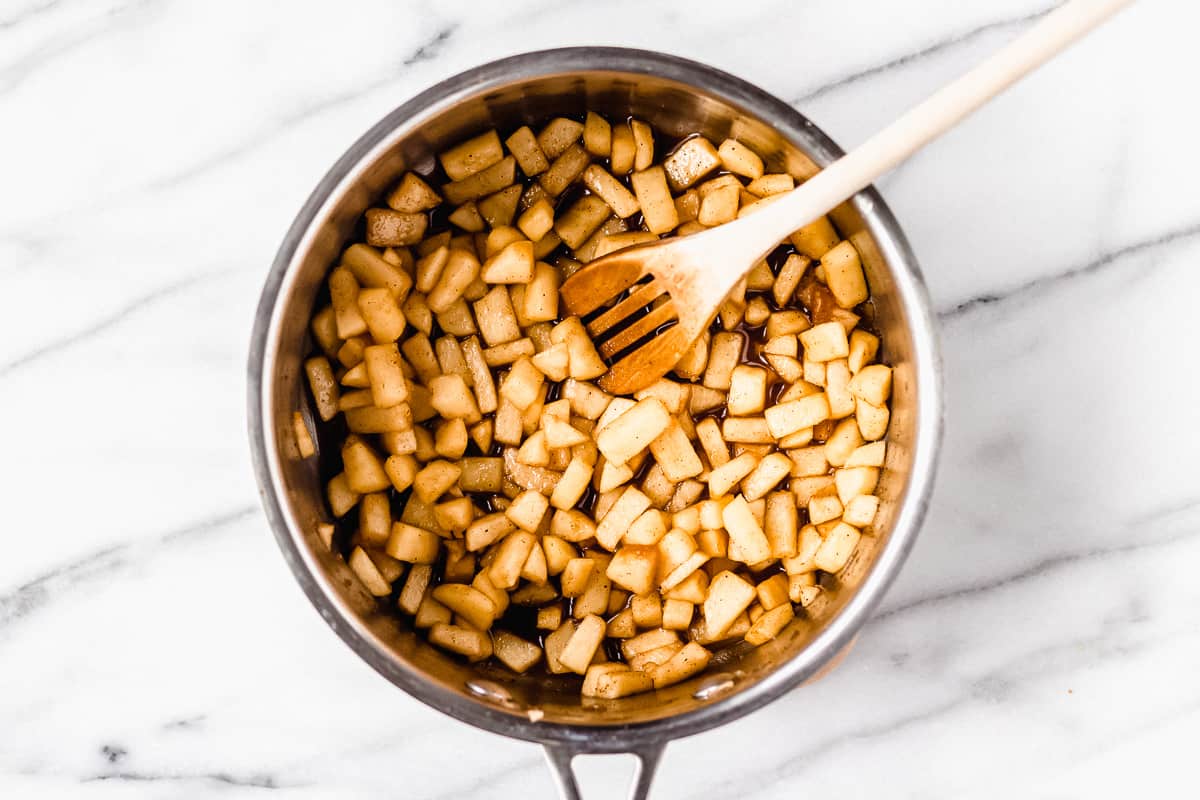 Diced apples and spices cooking in a sauce pan with a wood spoon