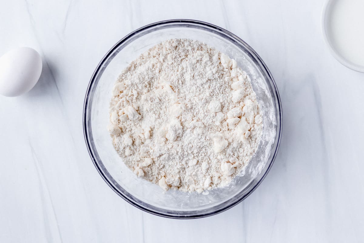Flour mixture with pea size bits of butter in it in a glass bowl on a white background
