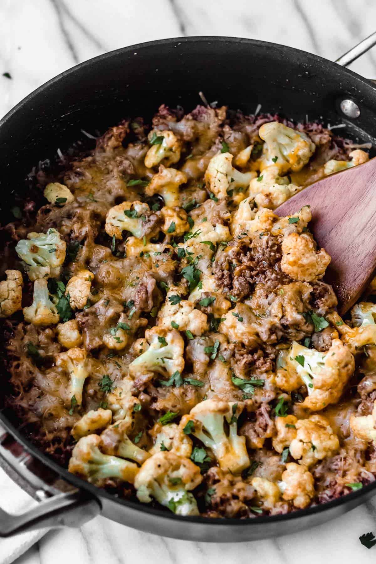 Keto Cheesy Barbecue Ground Beef and cauliflower skillet with a wood turner in it over a marble backdrop