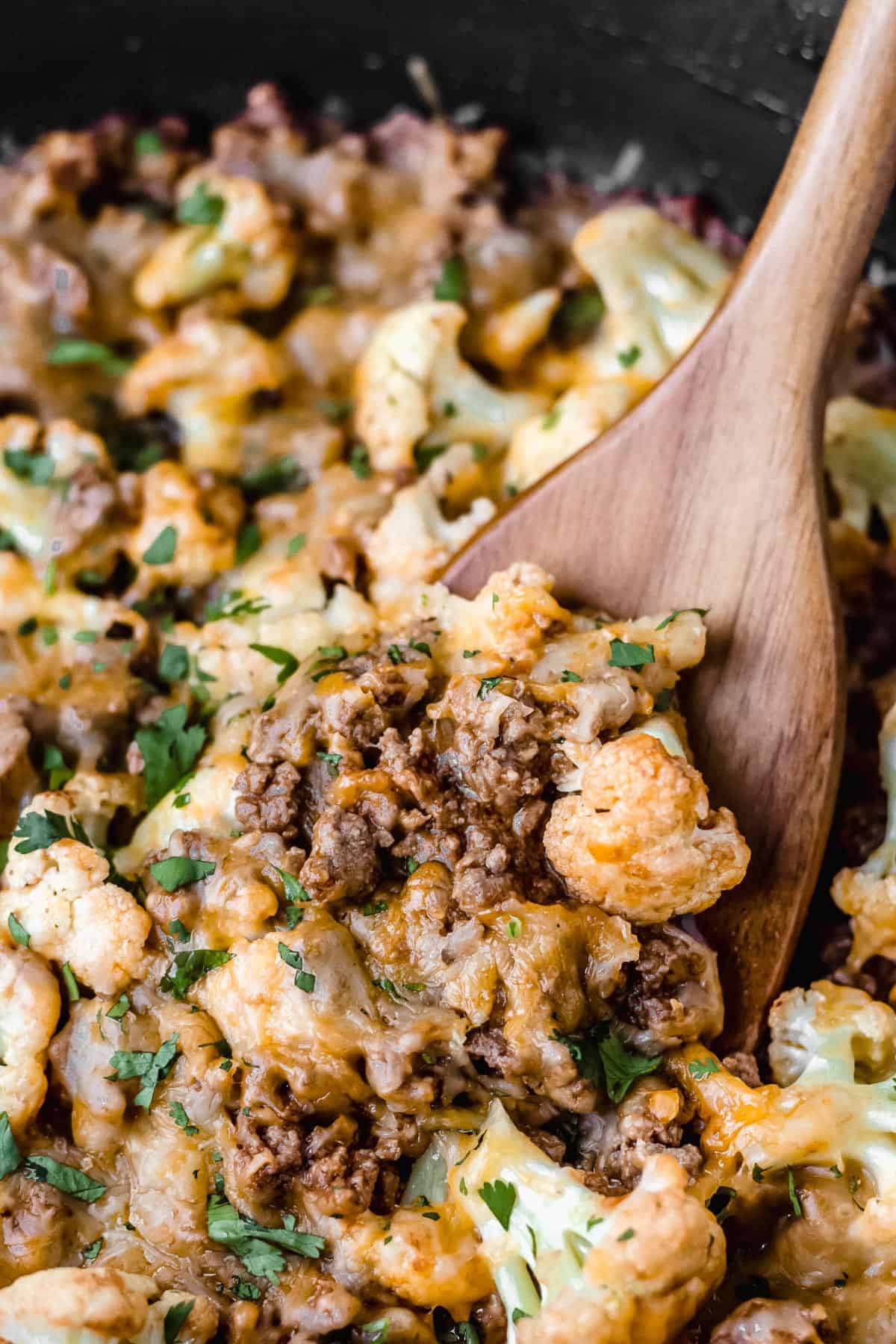 close up of a turner lifting up some keto cheesy barbecue ground beef and cauliflower in a black skillet