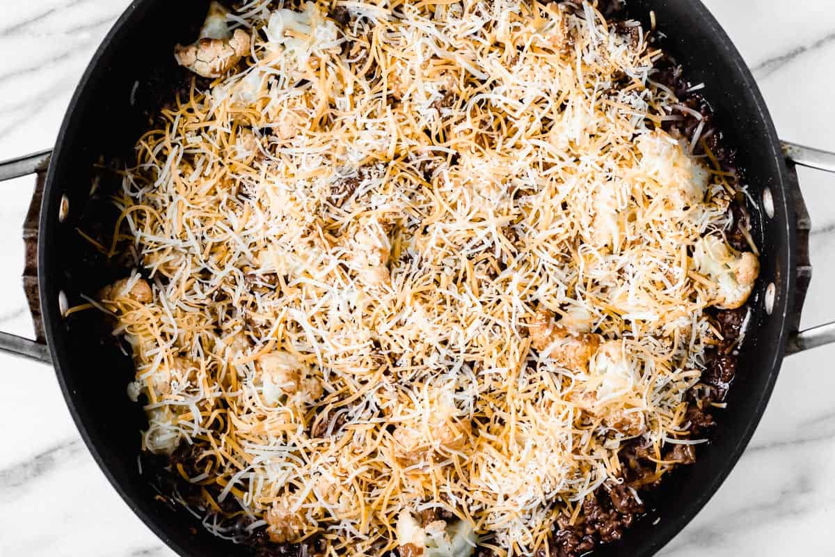 A skillet of beef and vegetables topped with shredded cheese