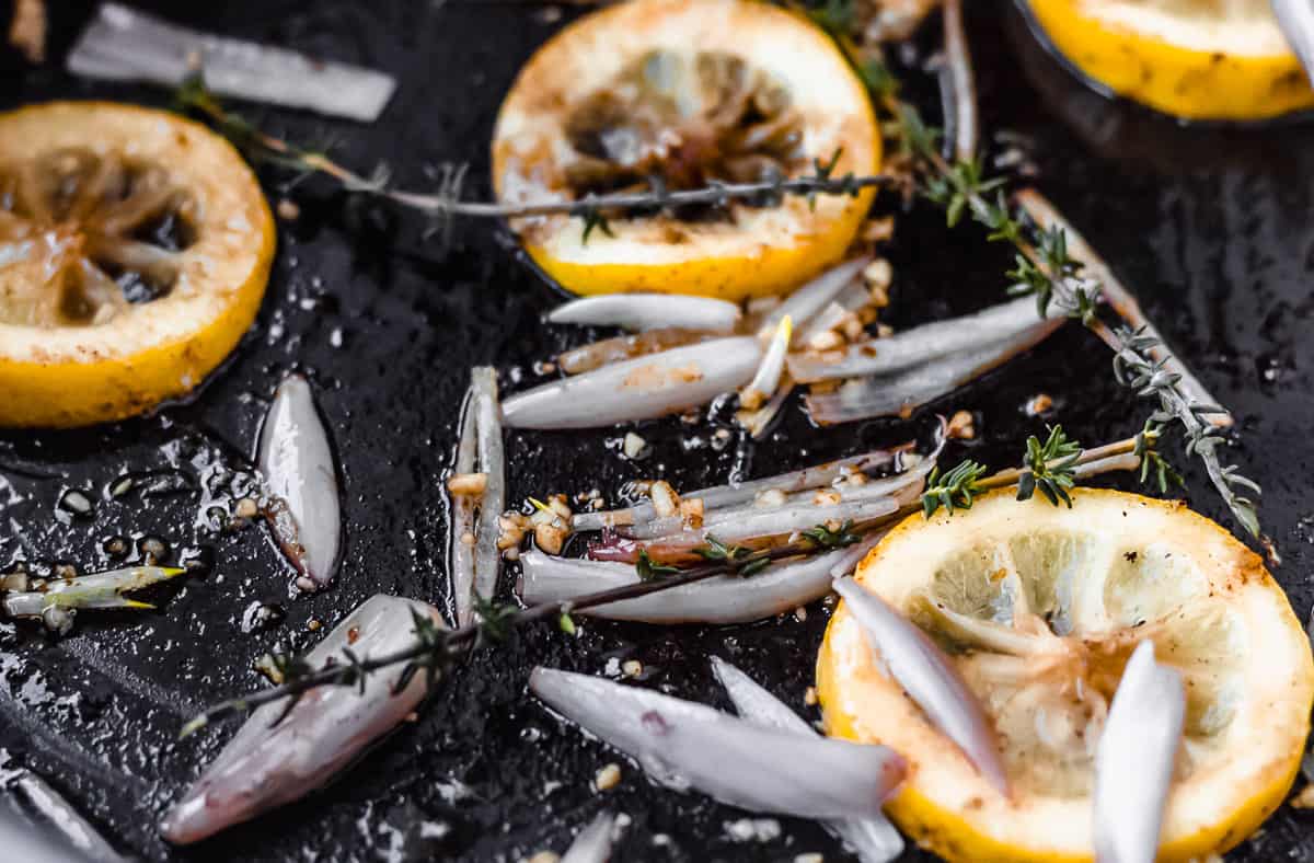 Lemons, shallots, garlic and butter close up in a black skillet