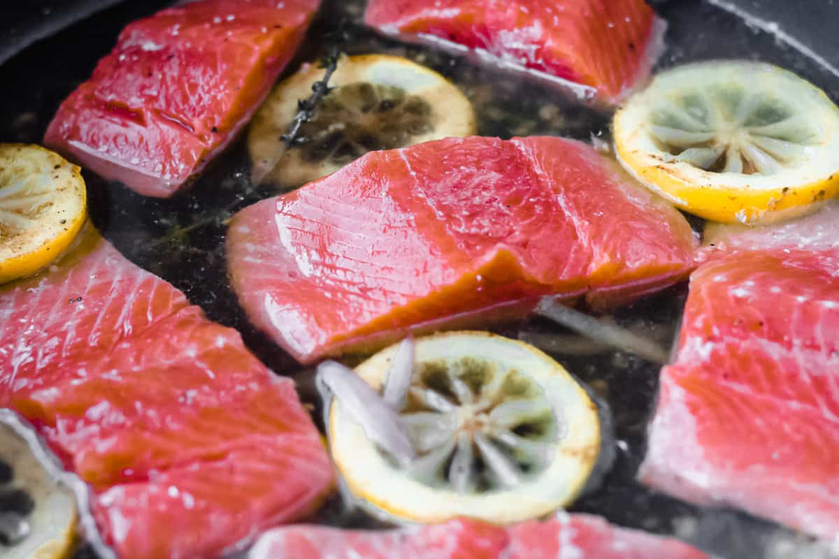 Salmon fillets with lemon slices and shallots in a black skillet