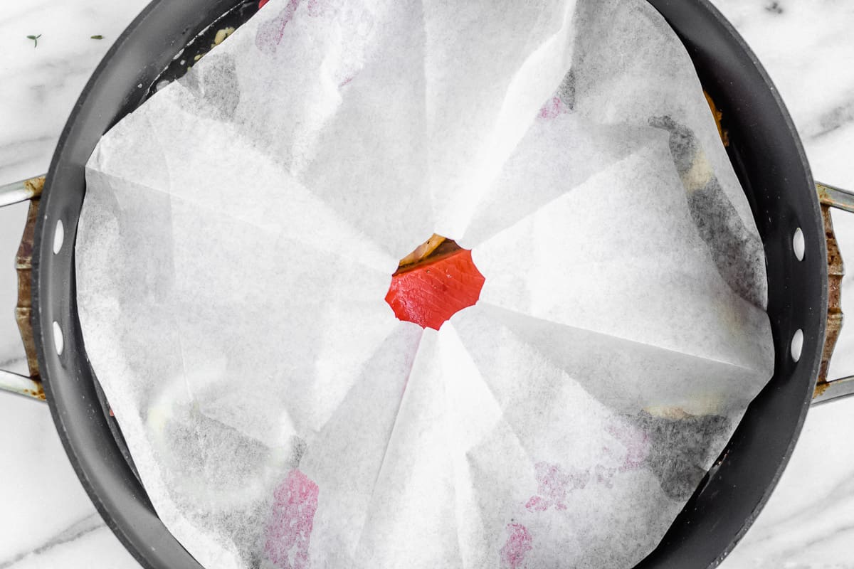 Salmon in a skillet covered with a parchment paper cartouche