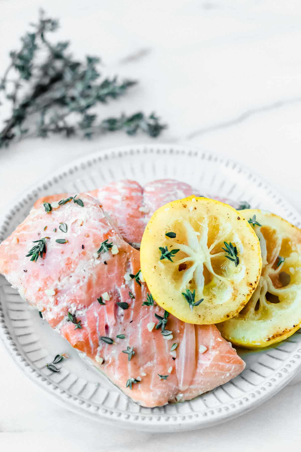 Poached salmon with lemon slices on a plate with a branch of fresh thyme in the background