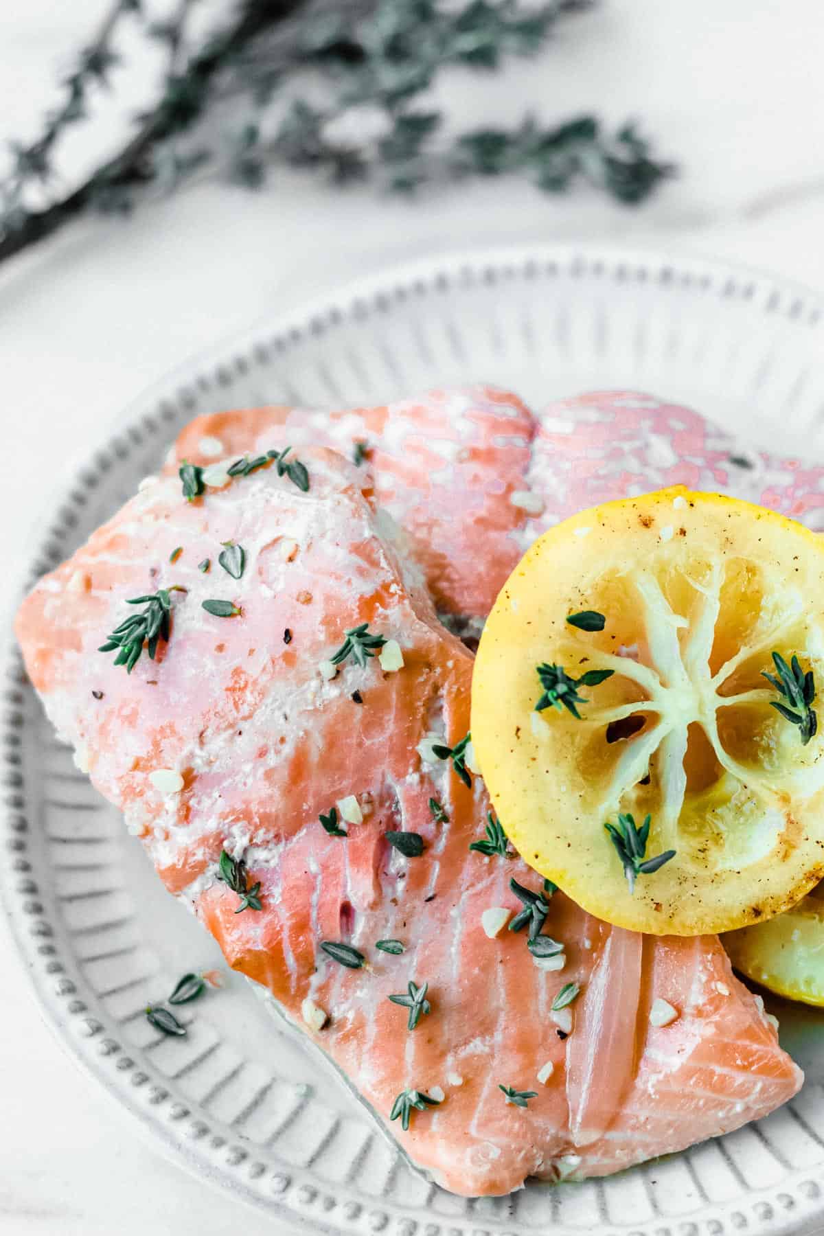 Close up of poached salmon and lemon slices with fresh thyme in the background