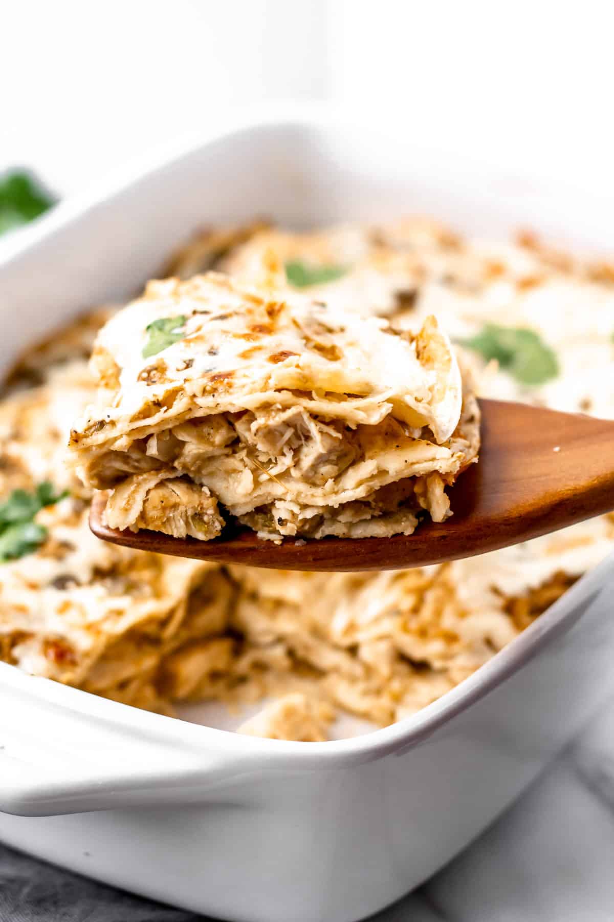 A serving of chicken enchilada casserole being lifted up with a wood turner