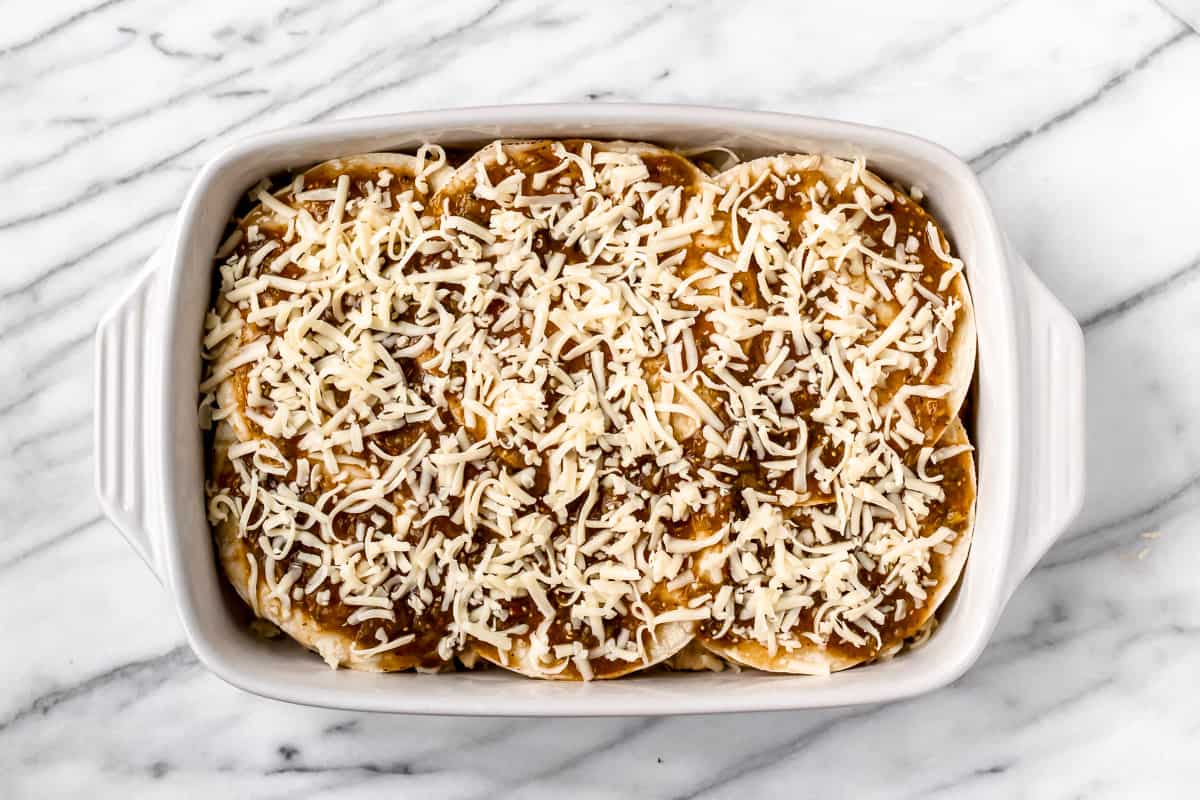 Chicken enchilada casserole prior to baking with cheese and green enchilada sauce on top of corn tortillas