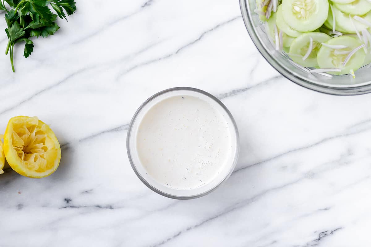 Cucumber salad dressing in a small glass bowl with other ingredients around it