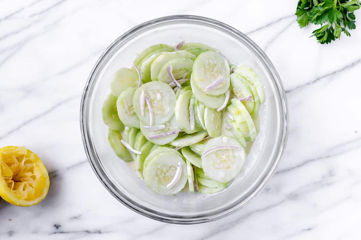 Cucumber salad in a glass bowl with parsley and lemon on a marble background