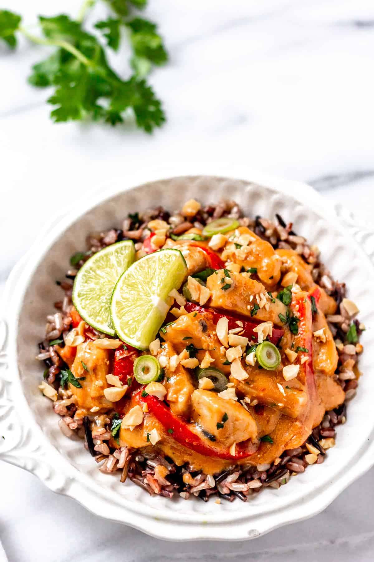 A white bowl filled with peanut butter chicken with cilantro leaves in the background