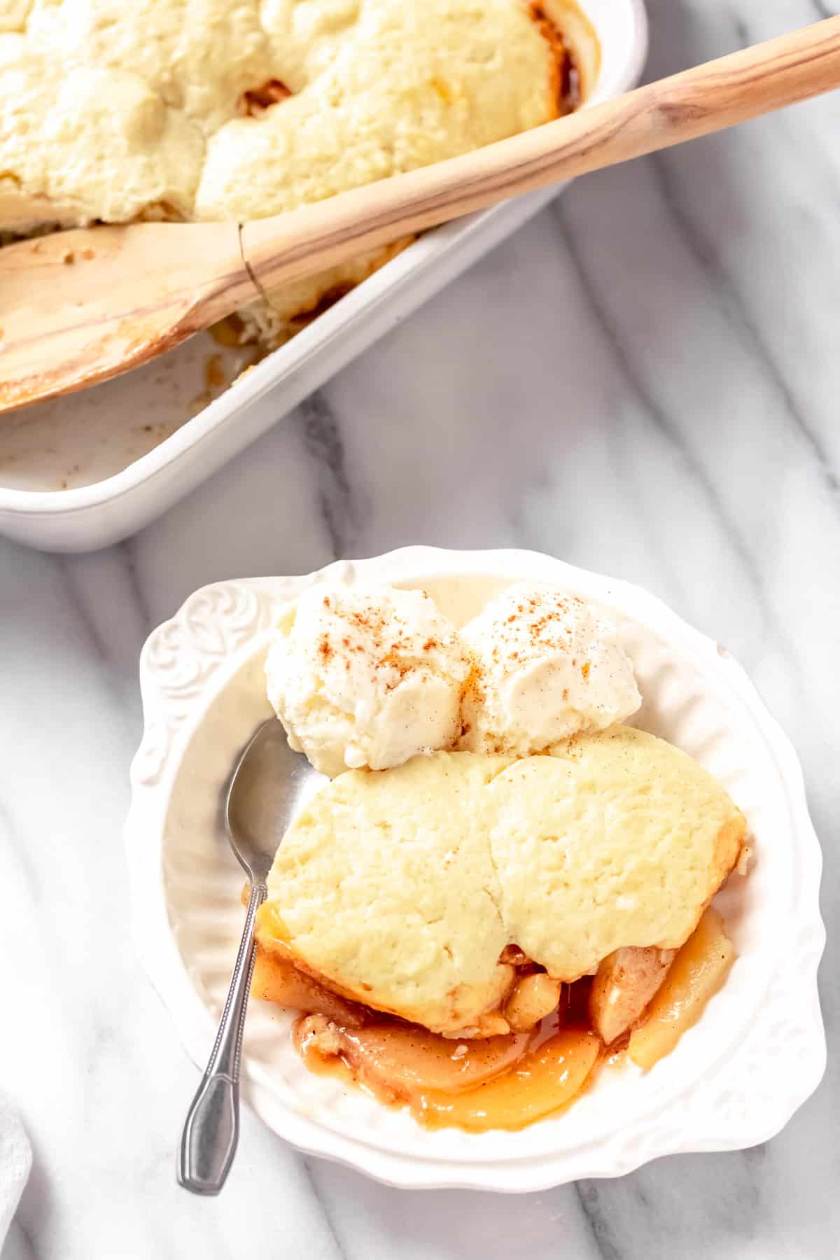 Pear cobbler and ice cream in a bowl with a spoon and a baking dish partially showing in the background