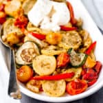 Close up of roasted summer vegetables on a white serving tray with a spoon