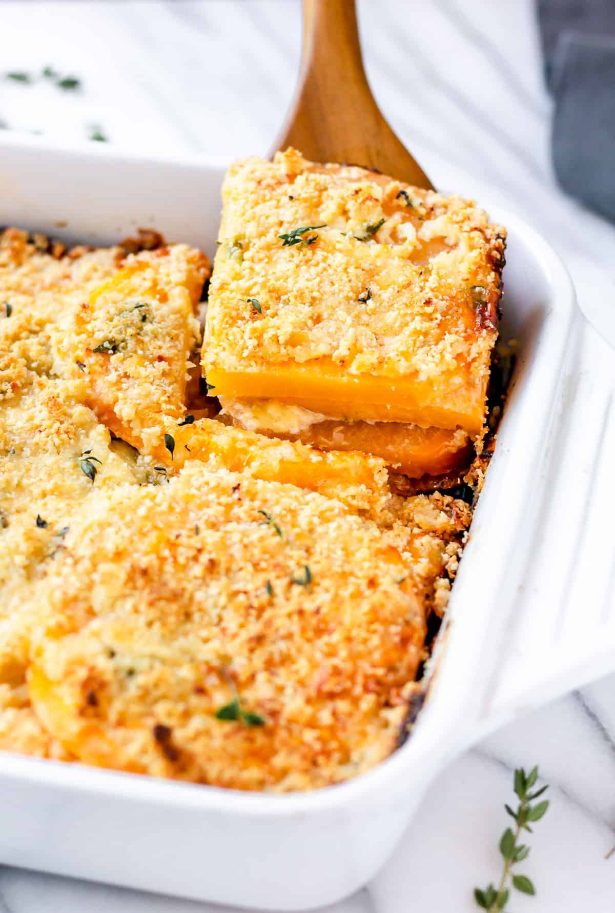 A serving of rutabaga gratin being lifted up out of a white baking dish