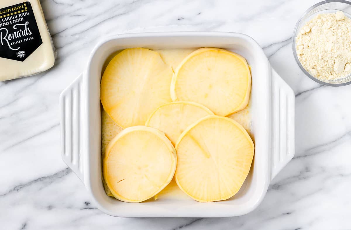 Slices of rutabaga in the bottom of a white, square baking dish