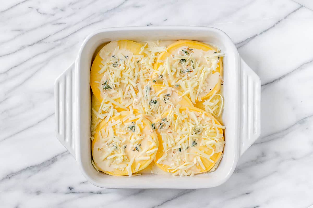 Slices of rutabaga with a cream mixture and grated cheese on top in a white, square baking dish