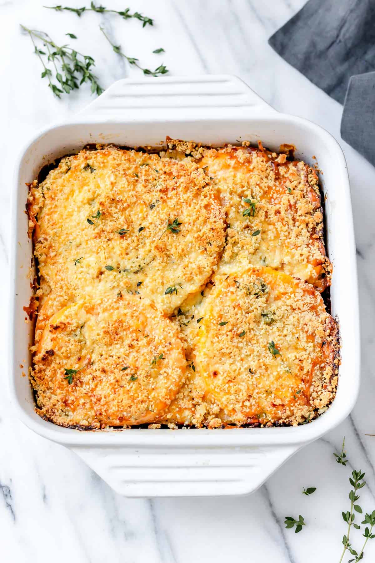 Overhead of rutabaga gratin in a white, square baking dish, with fresh sprigs of thyme around it on a marble backdrop