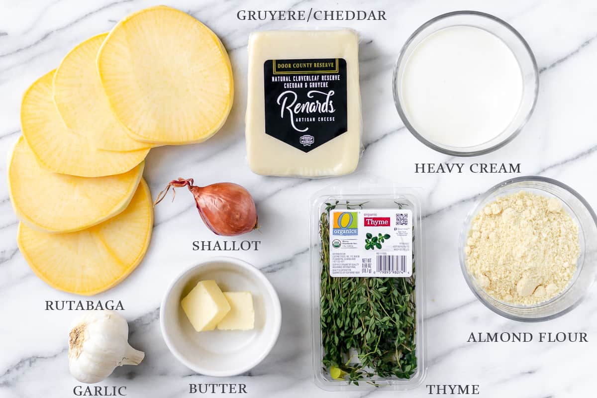 Ingredients needed to make rutabaga gratin on a marble backdrop with labels